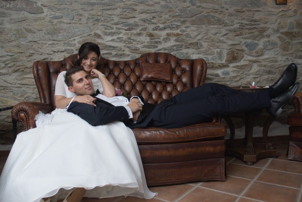 Braut und Bräutigam sitzen auf einer eleganten Ledercouch im Hochzeitsoutfit.