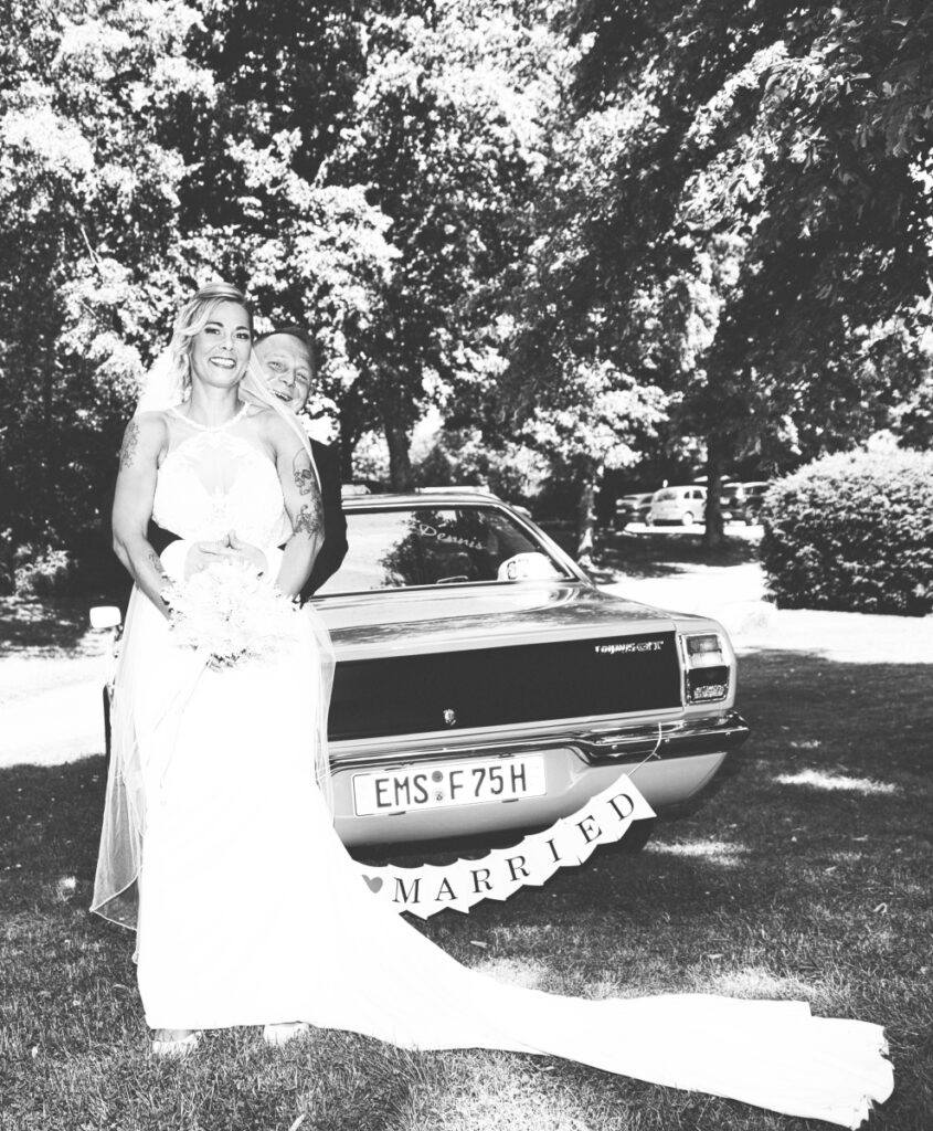 Brautpaar lehnt an Ford Taunus Hochzeitsauto mit Just Married Schild in Sankt Goarshausen
